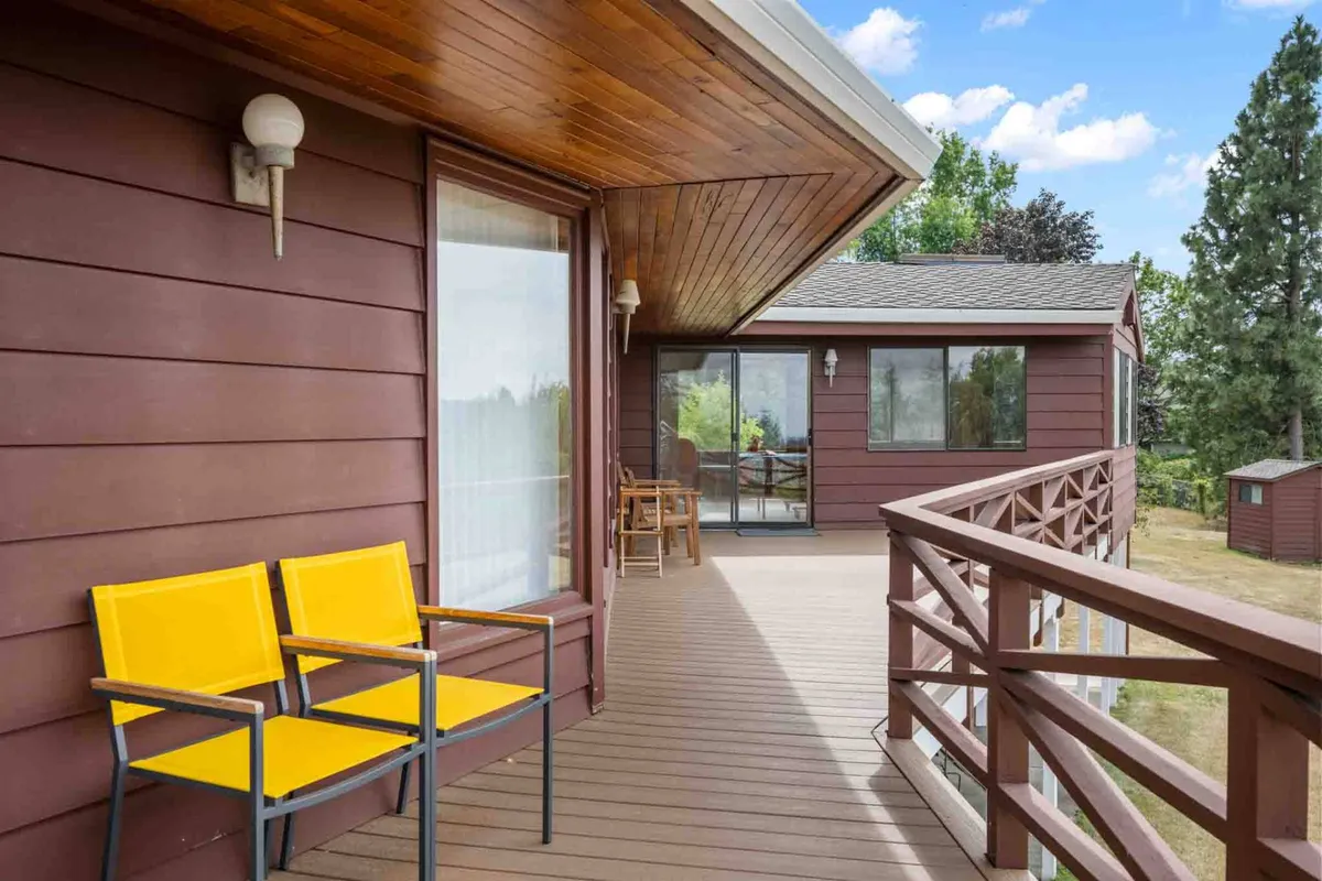 This exterior image features a wooden deck with cheerful yellow chairs, a sturdy wooden railing, and large windows looking into the home. The outdoor seating area suggests a connection to nature and ample space to relax after a day of adventure, while the windows hint at the spaciousness and welcome of the property.