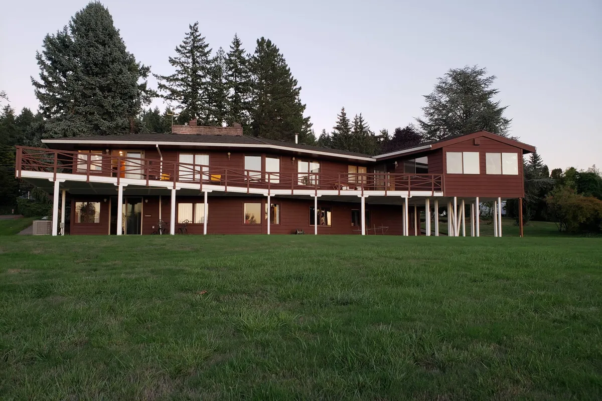 This image shows the home's modern wooden architecture with a large deck area opening directly onto an expansive lawn surrounded by trees. The inviting outdoor space makes it easy for residents and their pets to access the yard, relax together, and enjoy fresh air. The scene conveys a serene atmosphere, ideal for pet-friendly living.
