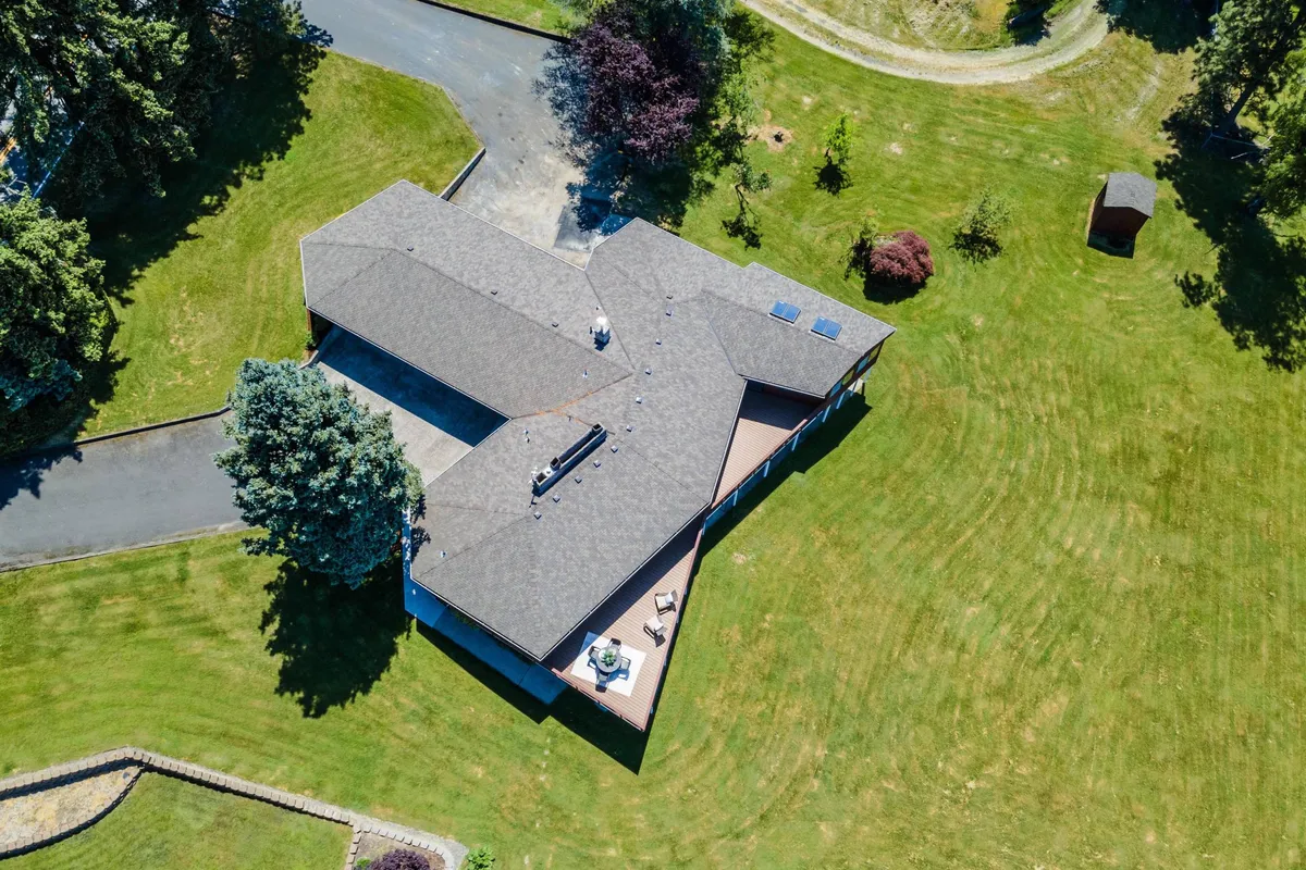 A wide exterior view of the property, showcasing a large, open yard with lush green grass and surrounding trees. The unique roofline of the home creates architectural interest, while the spaciousness of the yard is ideal for outdoor games, gatherings, and play. The natural setting suggests a safe, inviting place for families and pets to enjoy time outside together.
