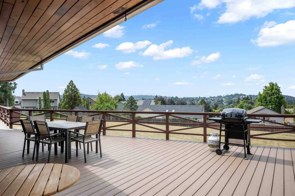 An inviting outdoor deck with a dining table set for a meal, a grill ready for barbecuing, and scenic views in the background. The spacious open area is ideal for gatherings, with the setting capturing the ambiance of relaxed outdoor dining and socializing as the sun sets.