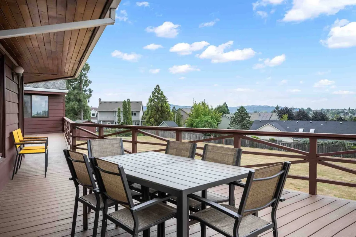 An exterior shot that features a large dining table with vibrant yellow chairs set on a patio, surrounded by greenery and distant mountains. The scene suggests opportunities for outdoor meals, family gatherings, and relaxation in a scenic environment, with enough space for everyone to spread out and enjoy nature.